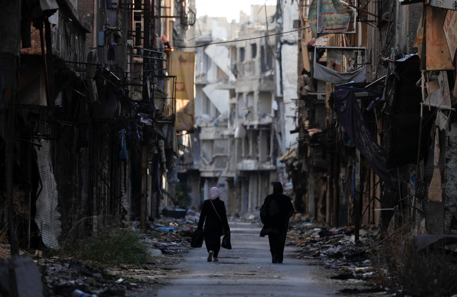 Women walk past damaged buildings at the Yarmouk Palestinian refugee camp on the southern outskirts of Damascus, Syria December 1, 2020. Picture taken December 1, 2020. REUTERS/Omar Sanadiki