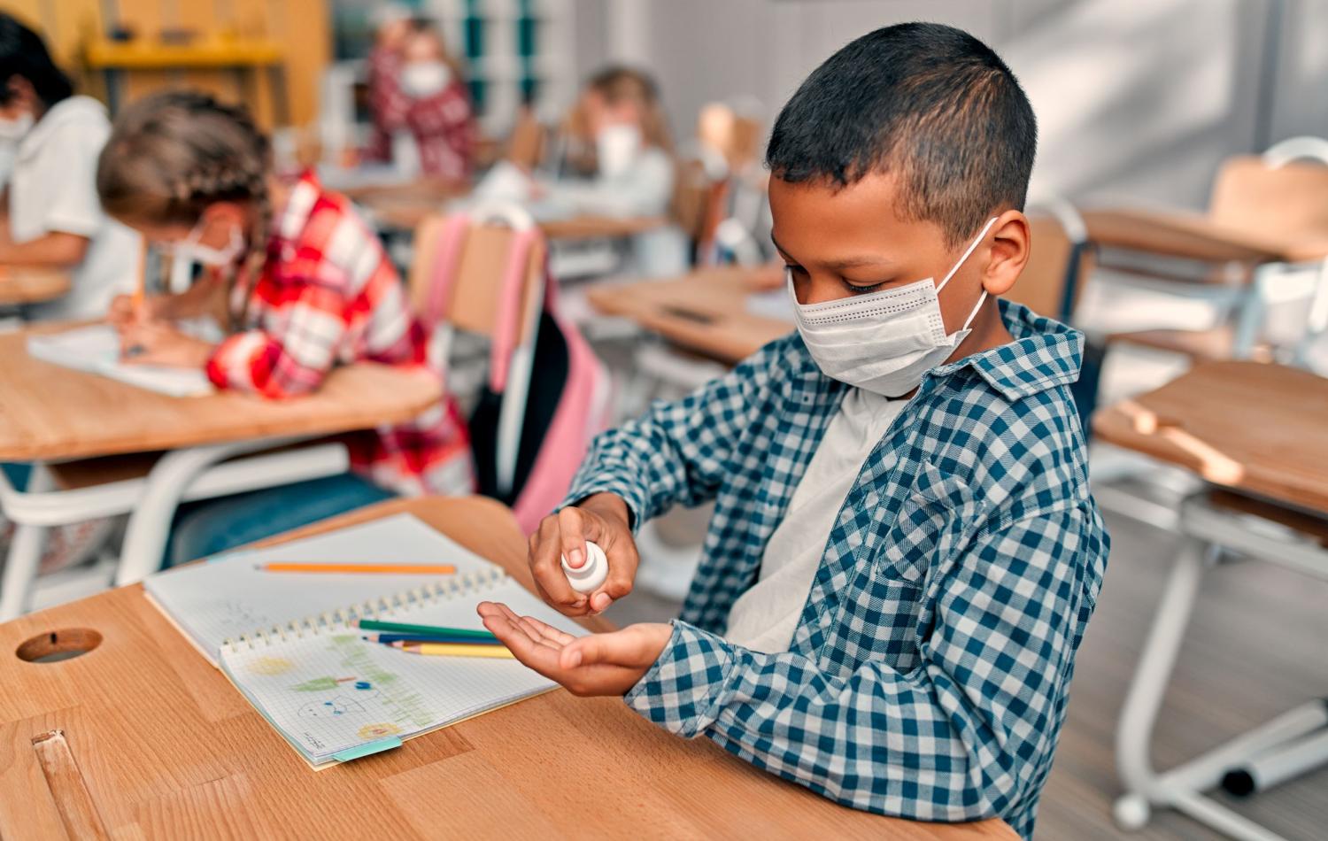 A male student uses hand sanitizer at his desk.