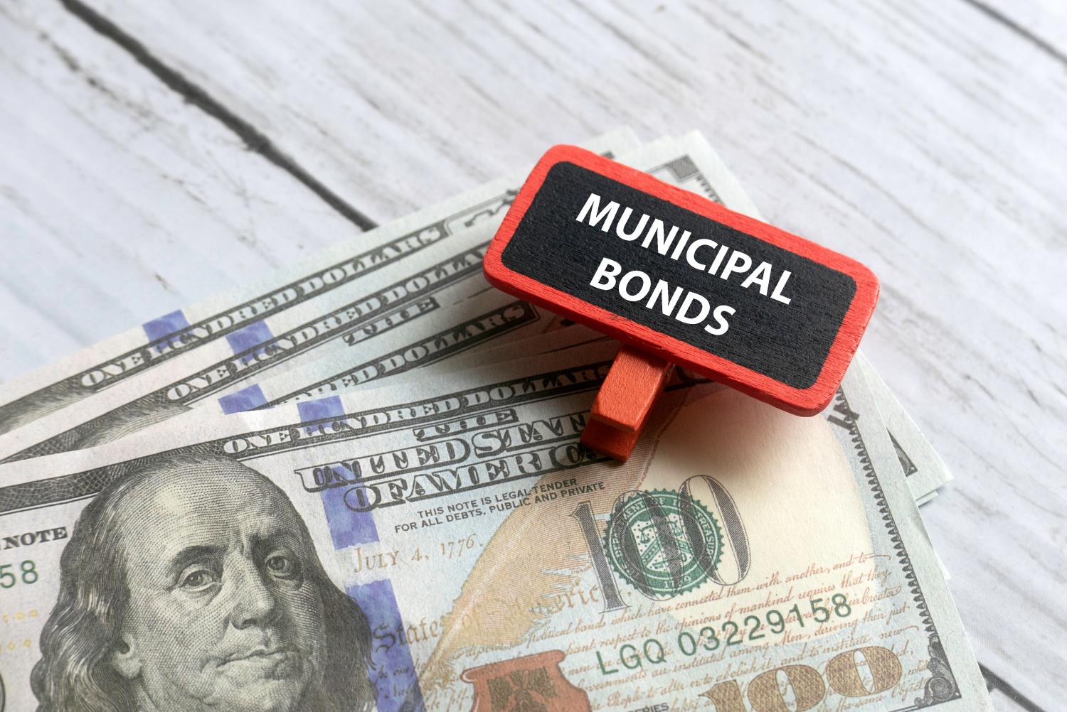 Selective focus of dollar notes and red tag written with MUNICIPAL BONDS on white wooden background.