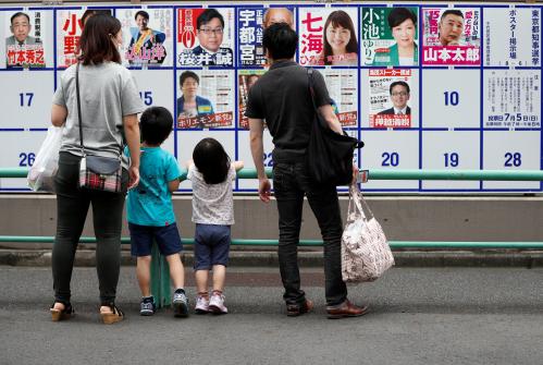 A family watches candidate posters, including current governor Yuriko Koike, for the Tokyo Governor election in front of a voting station amid the coronavirus disease (COVID-19) outbreak, in Tokyo, Japan July 5, 2020.  REUTERS/Issei Kato