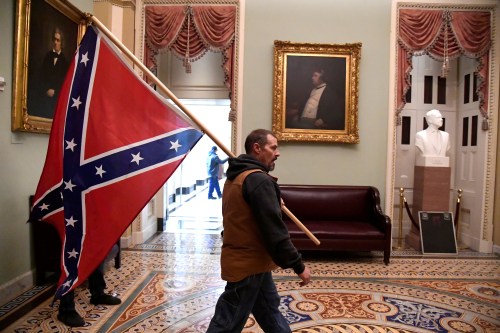A supporter of President Donald Trump carries a Confederate battle flag on the second floor of the U.S. Capitol near the entrance to the Senate after breaching security defenses, in Washington, U.S., January 6, 2021. A portrait of abolitionist senator Charles Sumner of Massachusetts, who was savagely beaten on the Senate floor after delivering a speech criticizing slavery in 1856, hangs above the couch.        REUTERS/Mike Theiler     TPX IMAGES OF THE DAY