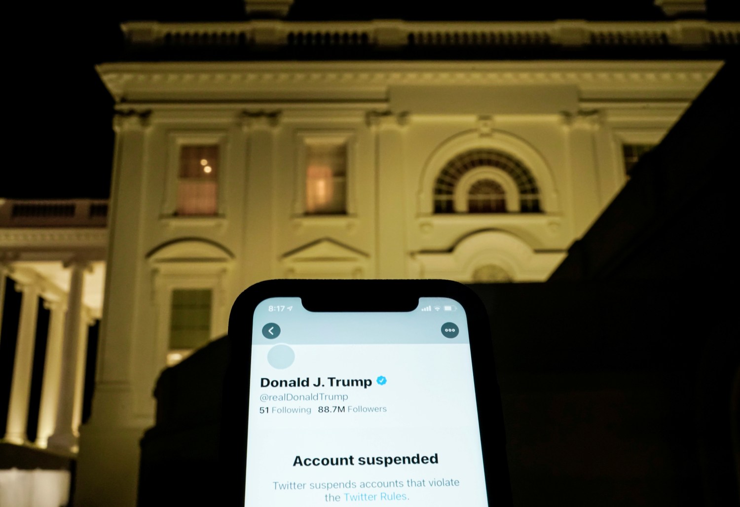 A photo illustration shows the suspended Twitter account of former President Donald Trump on a smartphone in front of the White House.