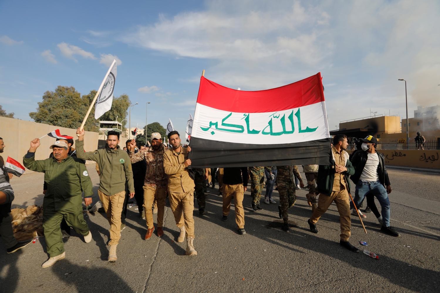 Protesters and militia fighters carry an Iraqi flag outside the U.S. Embassy during a protest to condemn air strikes on bases belonging to Hashd al-Shaabi (paramilitary forces), in Baghdad, Iraq January 1, 2020. REUTERS/Khalid al-Mousily