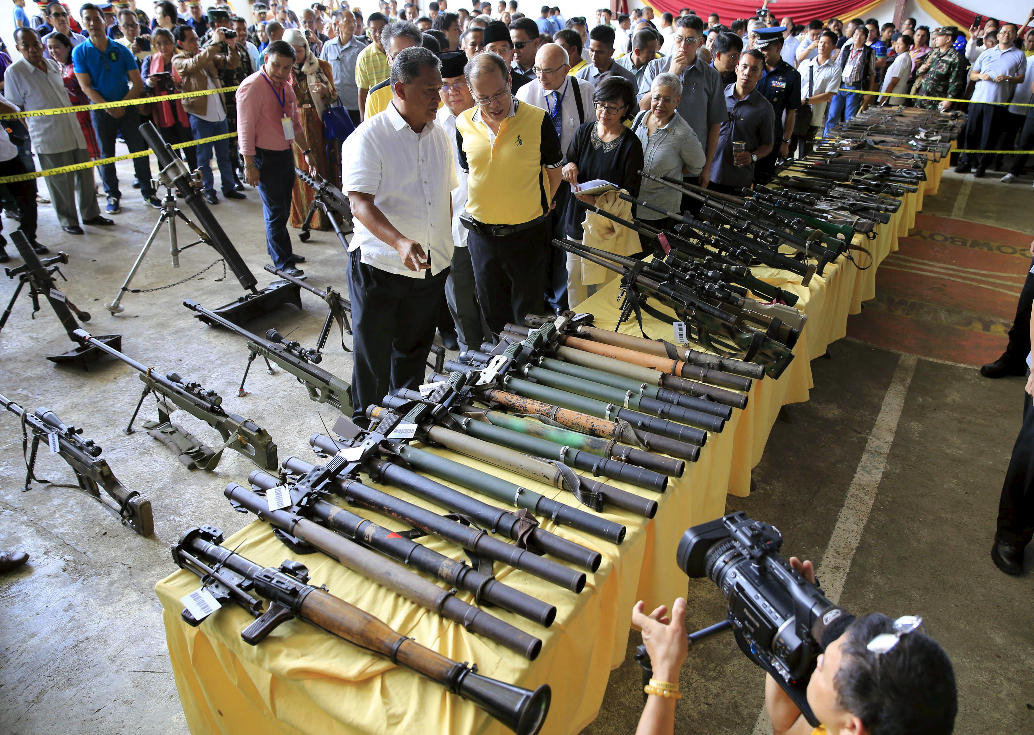 Philippine President Benigno Aquino (C) and Al-haj Murad Ebrahim (C, partially obscured), chairman of the Moro Islamic Liberation Front (MILF), look at weapons during the Ceremonial Turnover of Weapons and Decommissioning of MILF Combatants at the old capitol in Simuay town of Sultan Kudarat, Maguindanao province, southern Philippines June 16, 2015. Aquino attempted to revive a stalled peace process with Muslim insurgents on Tuesday, calling on lawmakers to grant autonomy for the predominantly Christian nation's restive southern region before time runs out. MILF handed in a token 75 weapons at the ceremony on Tuesday, where Aquino attempted to push forward his autonomy proposal for the region, known as Bangsamoro.     REUTERS/Romeo Ranoco