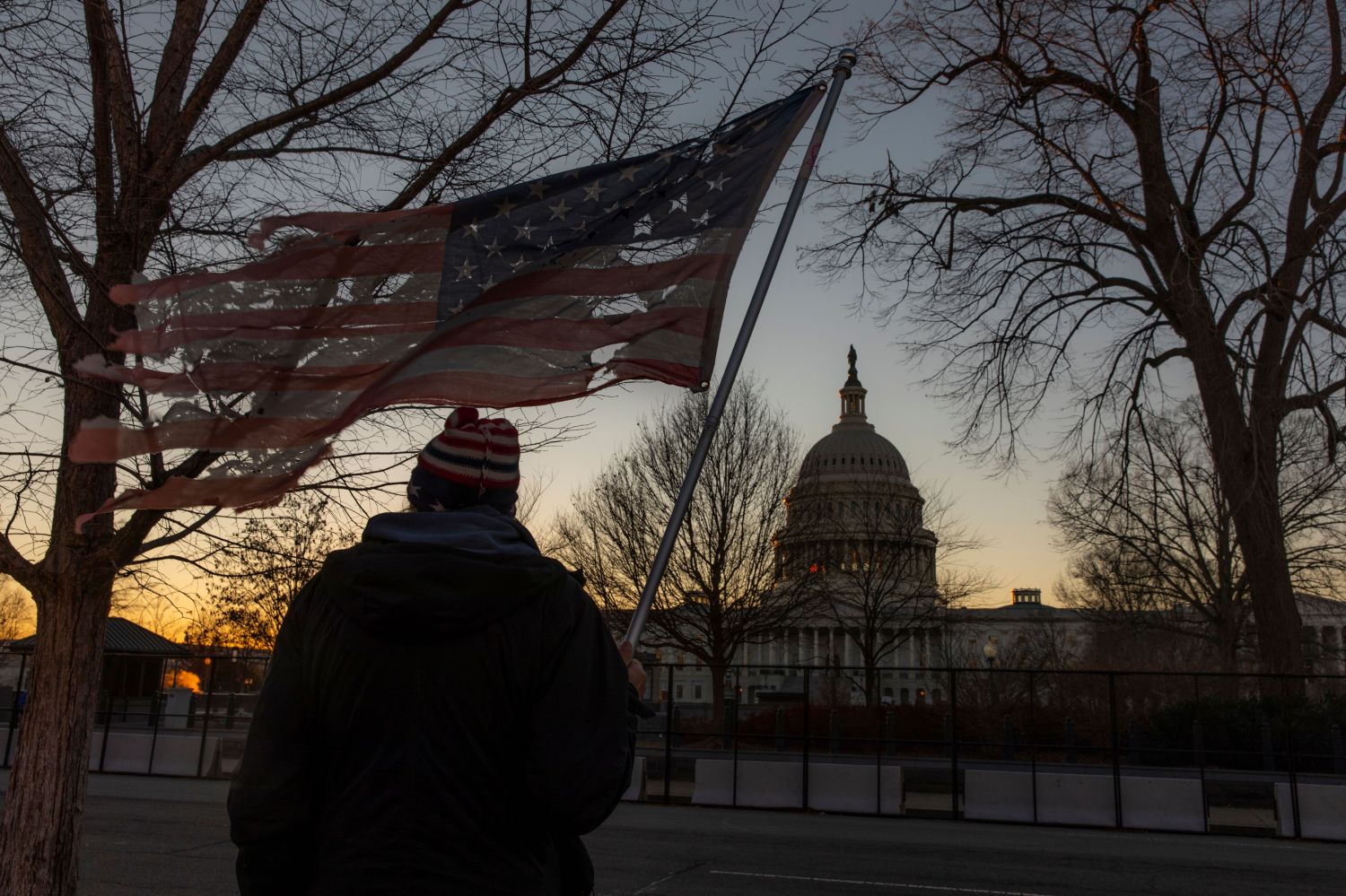 Washington DC, USA - January 9, 2021: A man with a flag watches as additional fencing is installed around the U.S. Capitol after the January 6 riots and ahead of President-Elect Biden's Inauguration.
