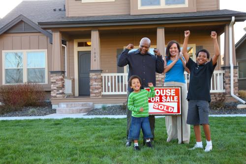 Family celebrating in front of house with for-sale sign