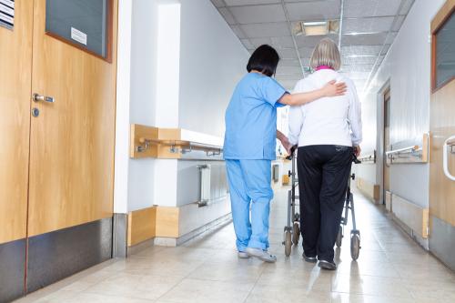 Nurse helping an older person in a nursing home hallway.