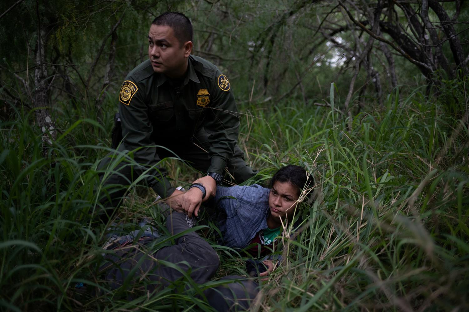 A border patrol agent apprehends a woman and a man after they were caught illegally crossing into the U.S. border from Mexico near McAllen, Texas, U.S., May 2, 2018. Reuters photographer Adrees Latif: "One could hardly tell there were people lying in the brush even as a U.S. Border Patrol agent stood over these migrants. They were tracked into the brush by their shoe prints. The group of nine had taken cover overnight and were apprehended the following morning for illegally crossing into the U.S. from Mexico." REUTERS/Adrees Latif  SEARCH "IMMIGRATION POY" FOR THIS STORY. SEARCH "REUTERS POY" FOR ALL BEST OF 2018 PACKAGES. TPX IMAGES OF THE DAY.