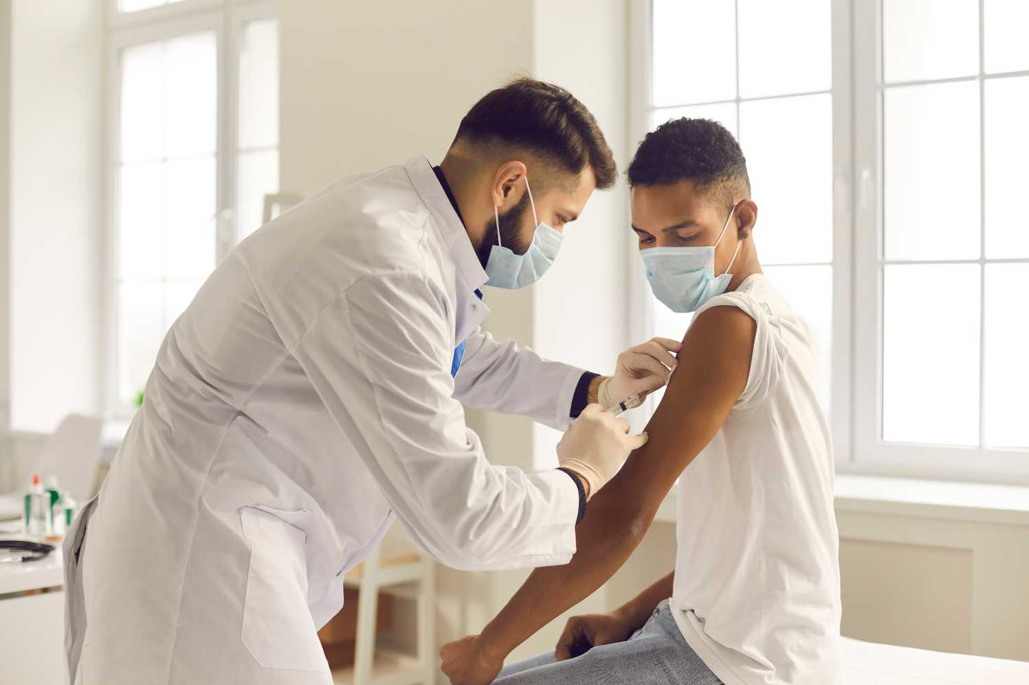 Doctor giving a shot to a patient, both wearing surgical masks.