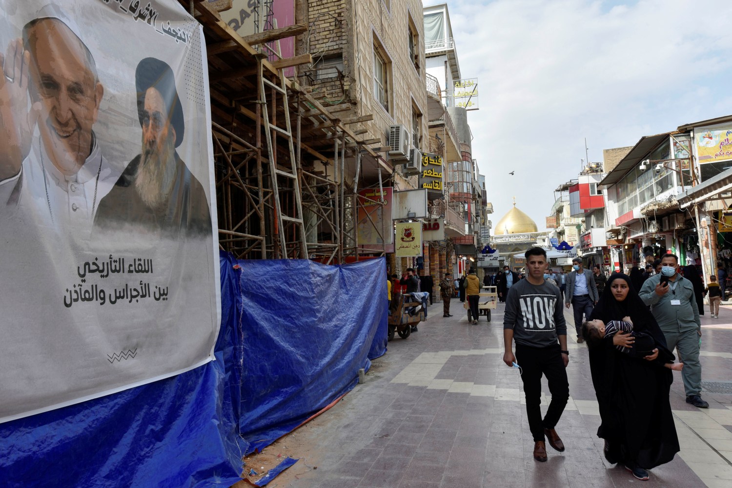 People walk past a poster of Pope Francis and Iraq's top Shi'ite cleric, Ayatollah Ali al-Sistani, ahead of the Pope's planned visit to Iraq, in Najaf, Iraq, March 4, 2021. REUTERS/ Alaa Al-Marjani