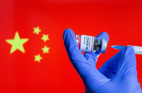 FILE PHOTO: A woman holds a small bottle labeled with a "Coronavirus COVID-19 Vaccine" sticker and a medical syringe in front of displayed China flag in this illustration taken, October 30, 2020. REUTERS/Dado Ruvic/File Photo