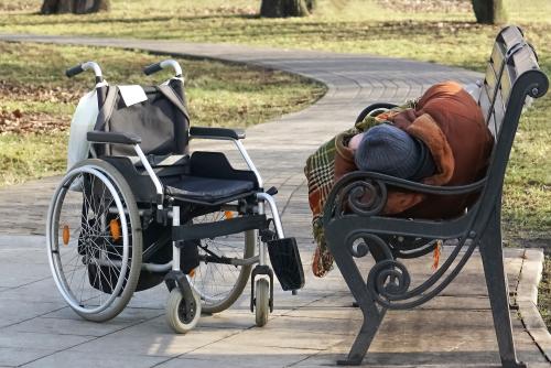 Person sleeping on a bench outside next to a wheelchair