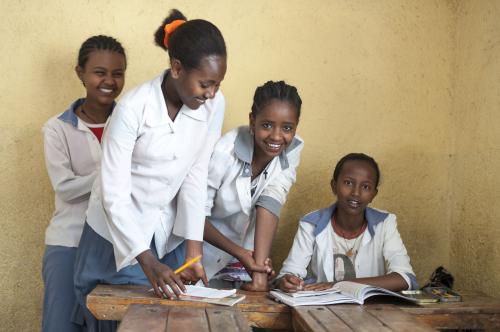 A female teacher and female students gather around a desk.