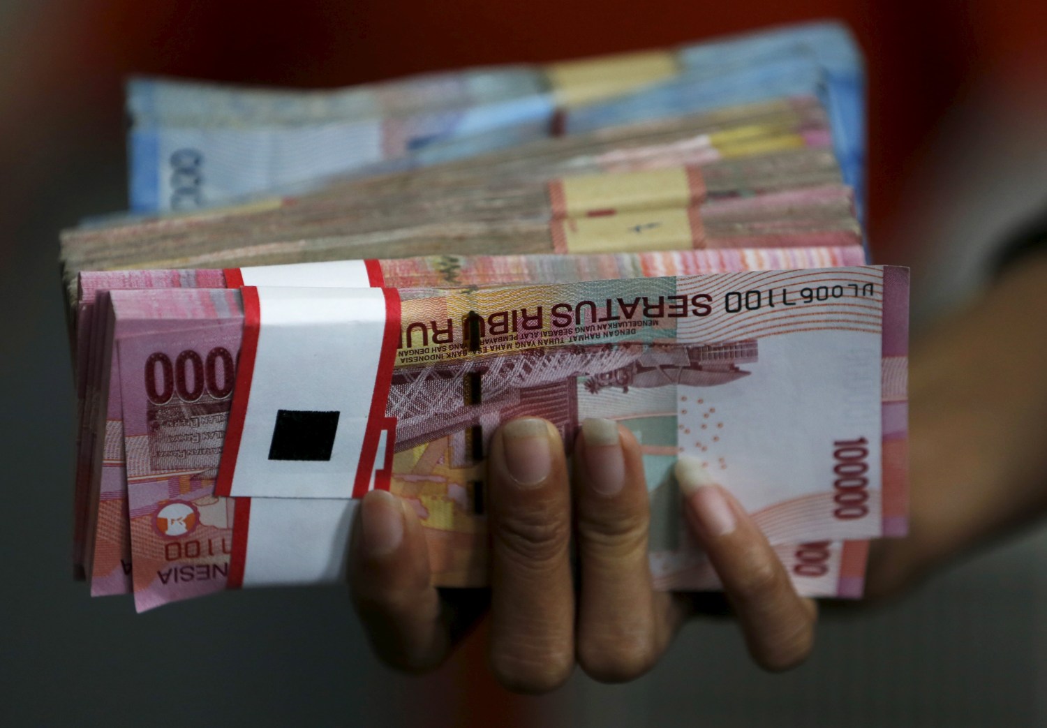 An employee of a money changer holds a stack of Indonesia rupiah notes before giving it to a customer in Jakarta, October 8, 2015. Most emerging Asian currencies dipped on Thursday as traders booked profits from recent gains and waited on minutes of the Federal Reserve's last policy meeting for any clues on the timing of a U.S. interest rate hike.  REUTERS/Beawiharta