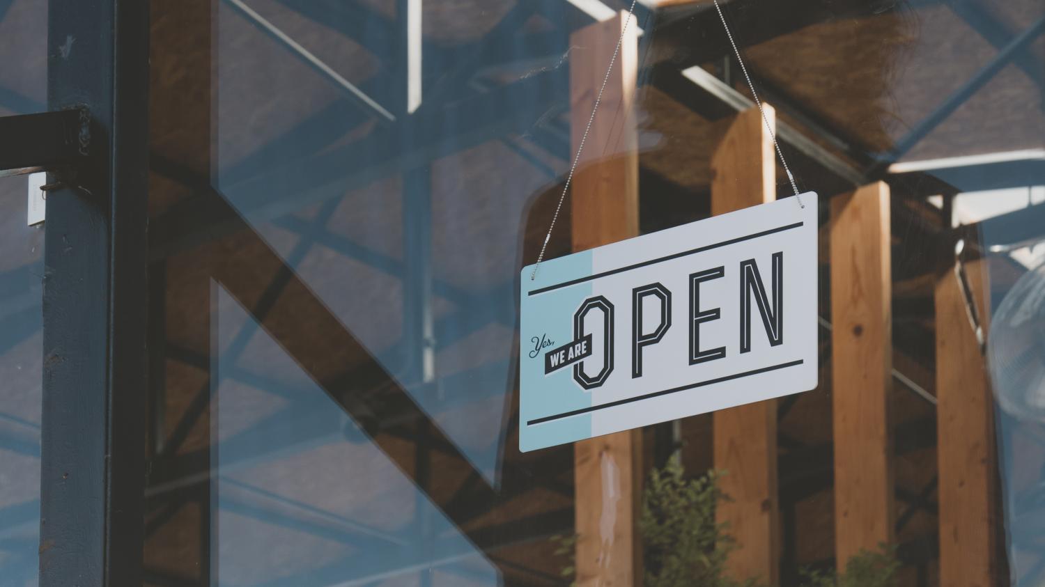 we are open sign hanging on the entrance door of a small cafe