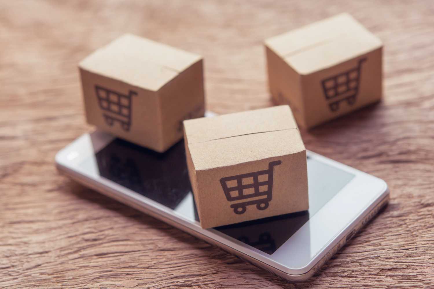 Online shopping - Paper cartons or parcel with a shopping cart logo and smartphone on wood table top