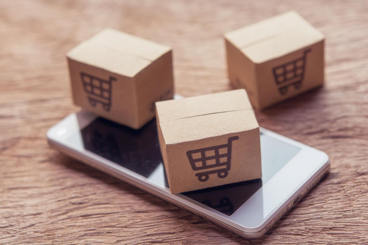 Online shopping - Paper cartons or parcel with a shopping cart logo and smartphone on wood table top