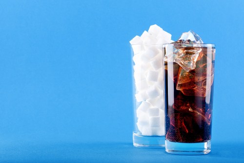 Glass of brown soda next to a glass full of sugar cubes