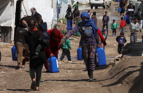 Syrian refugees walk as they carry containers at an informal tented settlement in the Bekaa valley, Lebanon March 12, 2021. Picture taken March 12, 2021. REUTERS/Mohamed Azakir