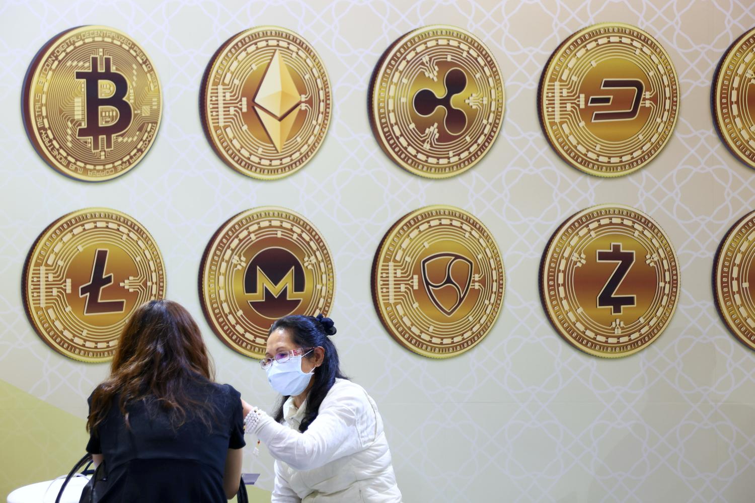 FILE PHOTO: Customers talk against a backboard with signs of cryptocurrency during 2020 Taipei International Finance Expo in Taipei, Taiwan, November 27, 2020. REUTERS/Ann Wang/File Photo