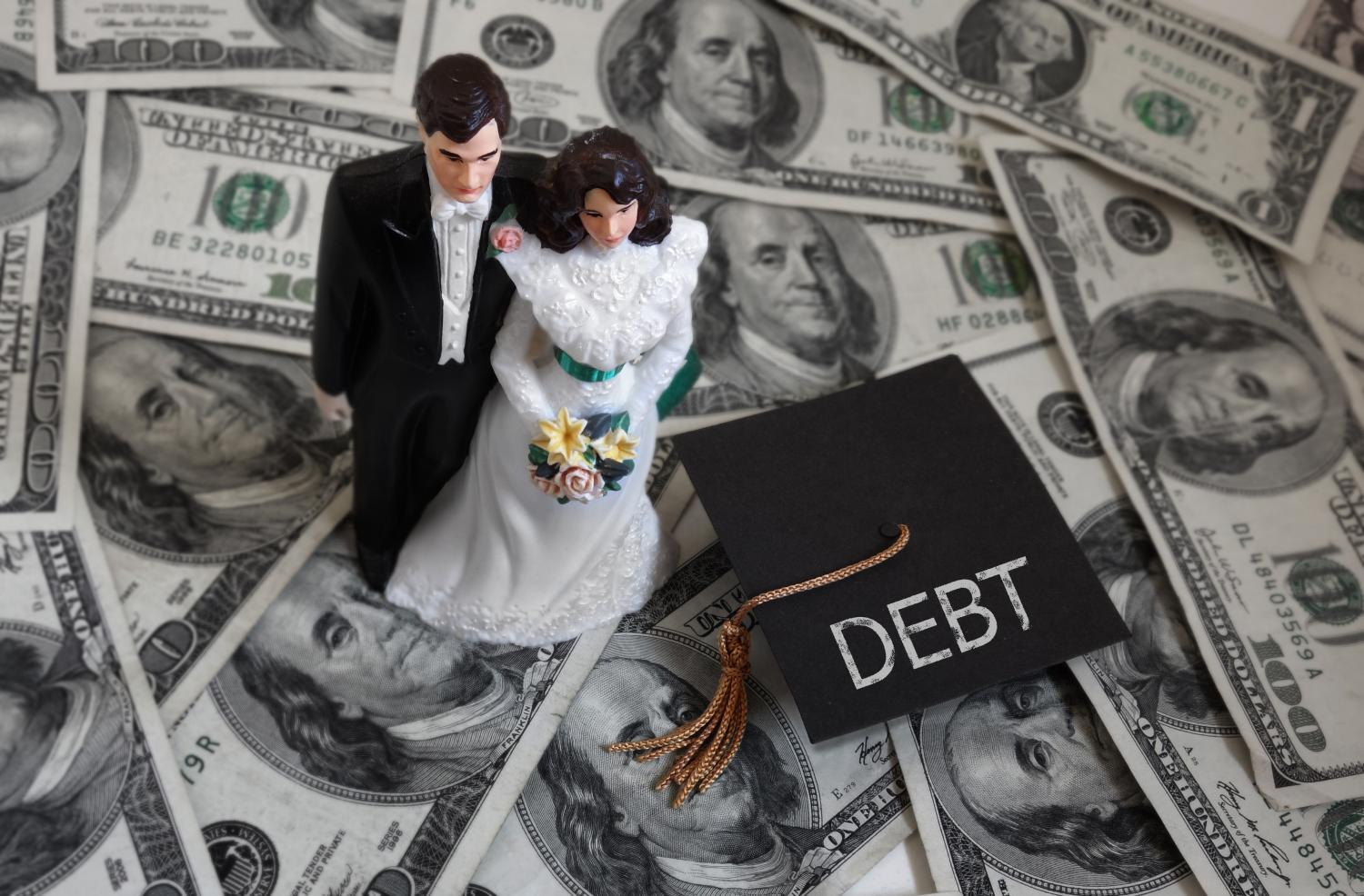 Newlyweds standing on a pile of money and next to a graduation cap that reads "debt"