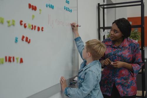 A teacher watches as a student writes on a white board.
