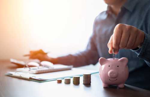 Person sitting at a desk putting a coin into a piggy bank