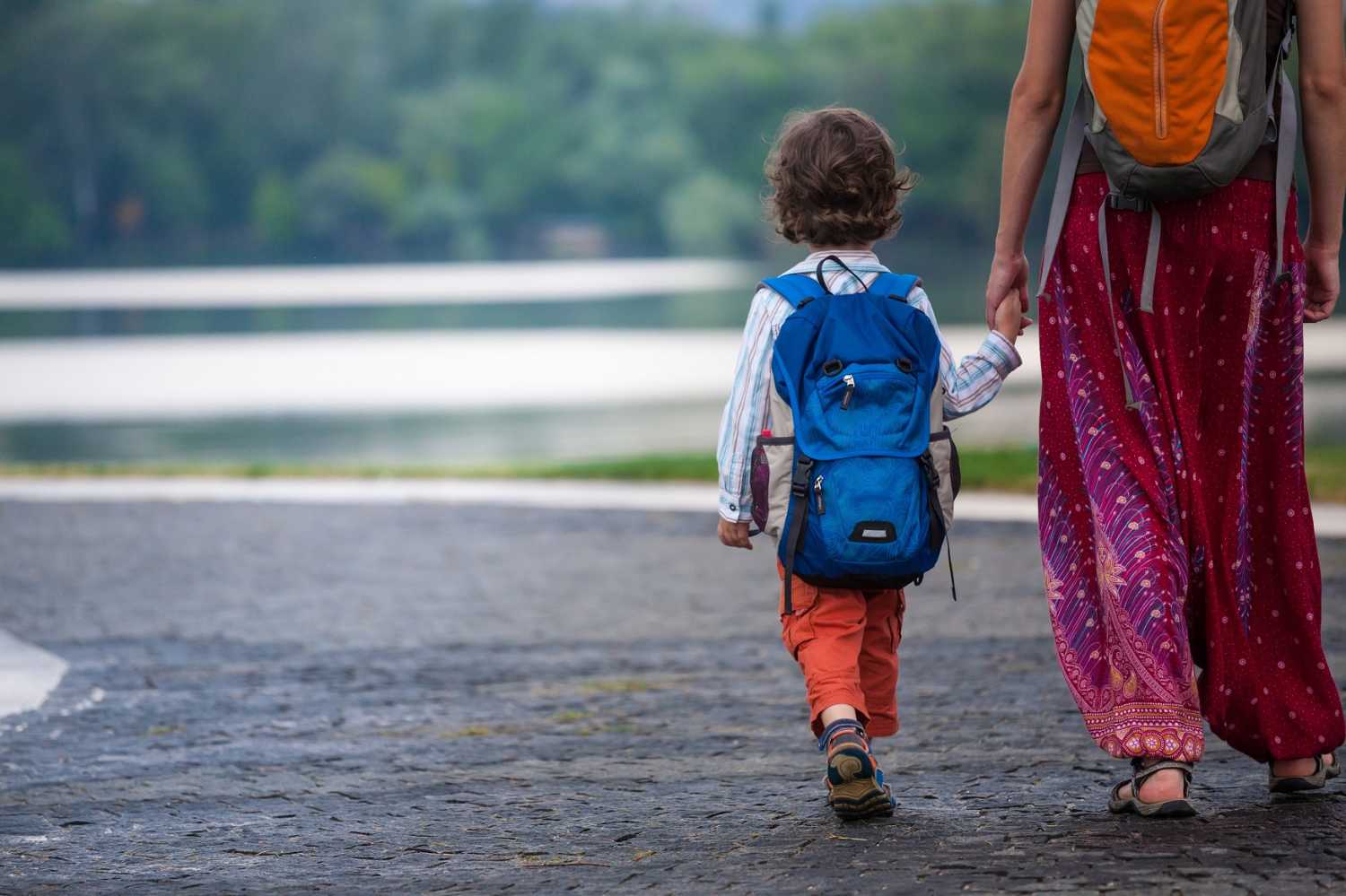 Young boy with backpack and mother walking down the road holding hands.