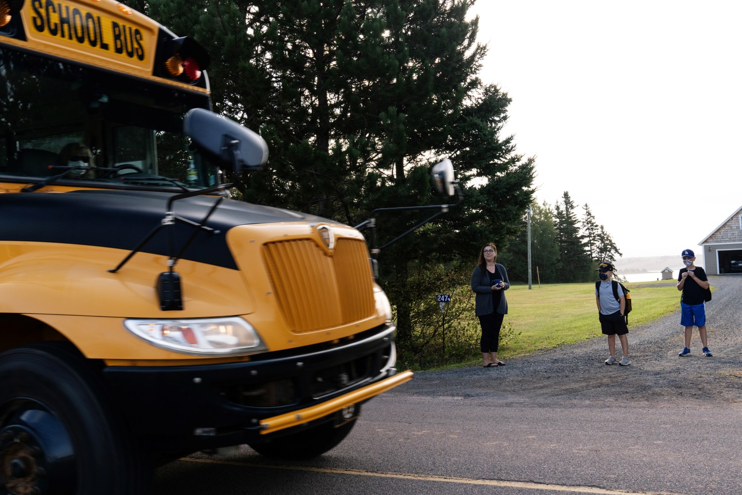 A school bus passes by as Monica Lee, Ronan Lee and Braydon Lee await their turn to load the bus as schools reopen with measures in place to prevent the spread of the coronavirus disease (COVID-19) in Vernon Bridge, Prince Edward Island, Canada September 8, 2020. REUTERS/John Morris