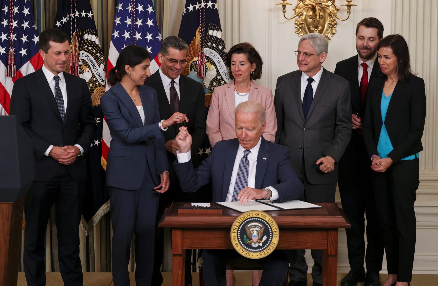 U.S. President Joe Biden hands a pen to Lina Khan, chair of the Federal Trade Commission, as he signs an executive order on "promoting competition in the American economy" as members of his Cabinet standby in the State Dining Room at the White House in Washington U.S., July 9, 2021. REUTERS/Evelyn Hockstein