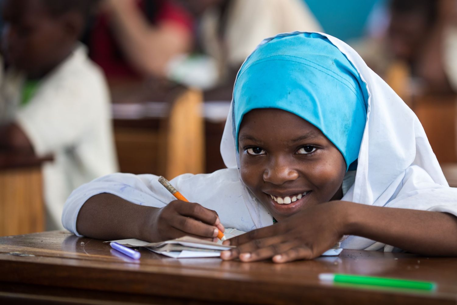 A girl in a classroom in Tanzania smiles at the camera.