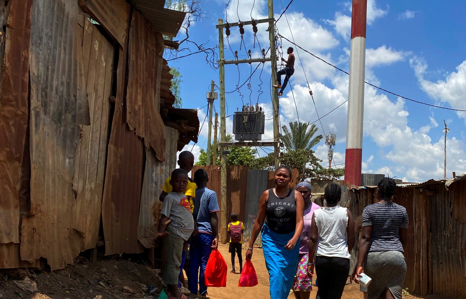 Residents walk through a walkway as a man connects electricity above the power transformer in a village in the Kibera slums in Nairobi, Kenya April 2, 2021. REUTERS/Thomas Mukoya