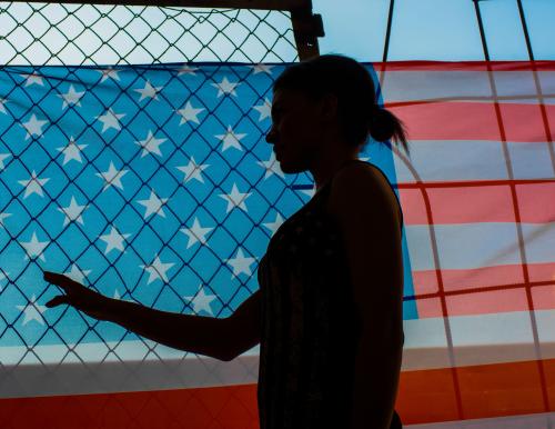 Silhouette of a woman in front of a fence and American flag