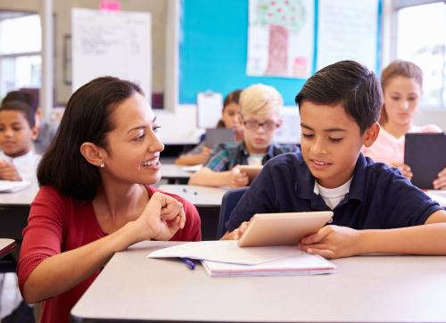 Teacher helping elementary school boy using tablet computer