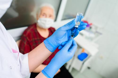 Doctor preparing a vaccine dose with an older woman in the background.