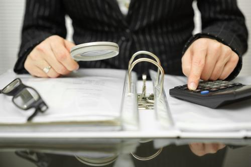 Person looking at records with calculator and magnifying glass.