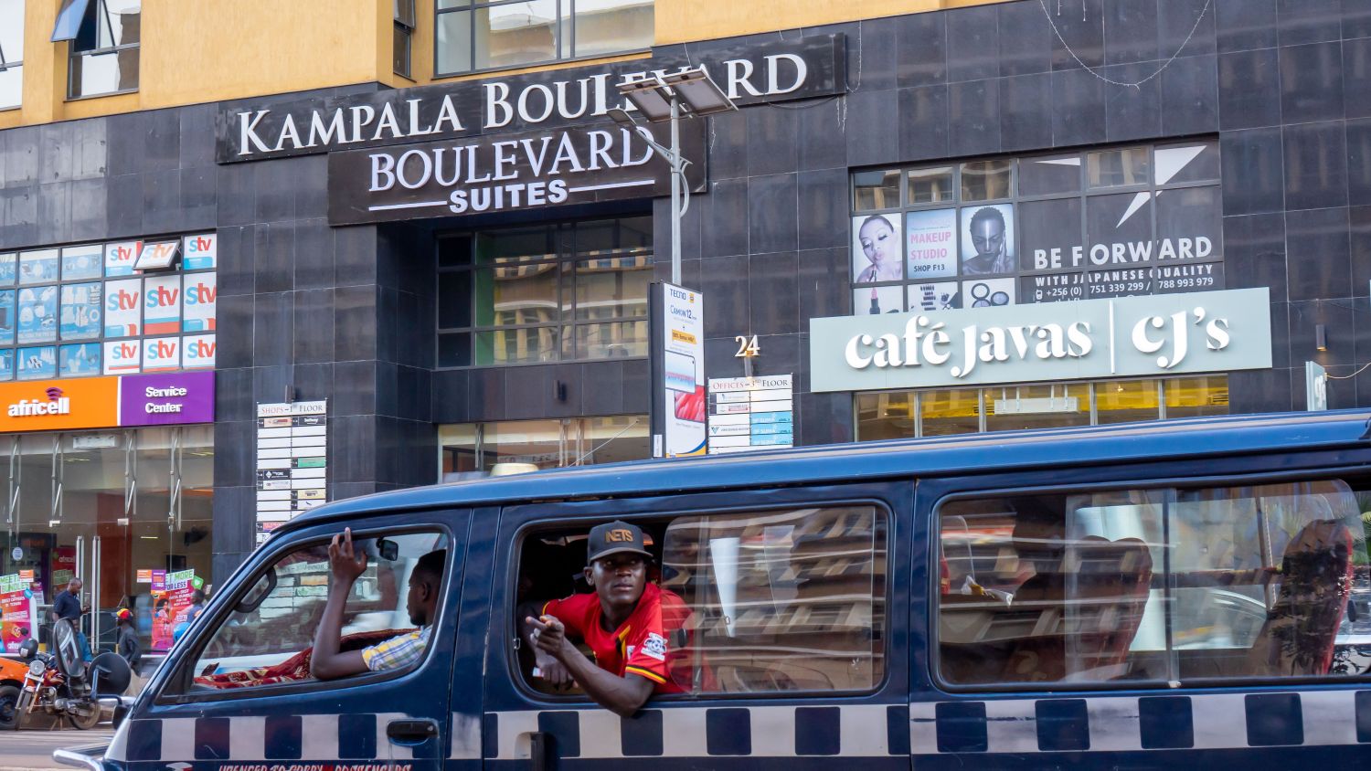 KAMPALA, UGANDA - JANUARY 05, 2020: A front view of Kampala Boulevard Suites, leading shopping mall and hotel with a foreground of an African man in a minibus, popular transportation for locals.