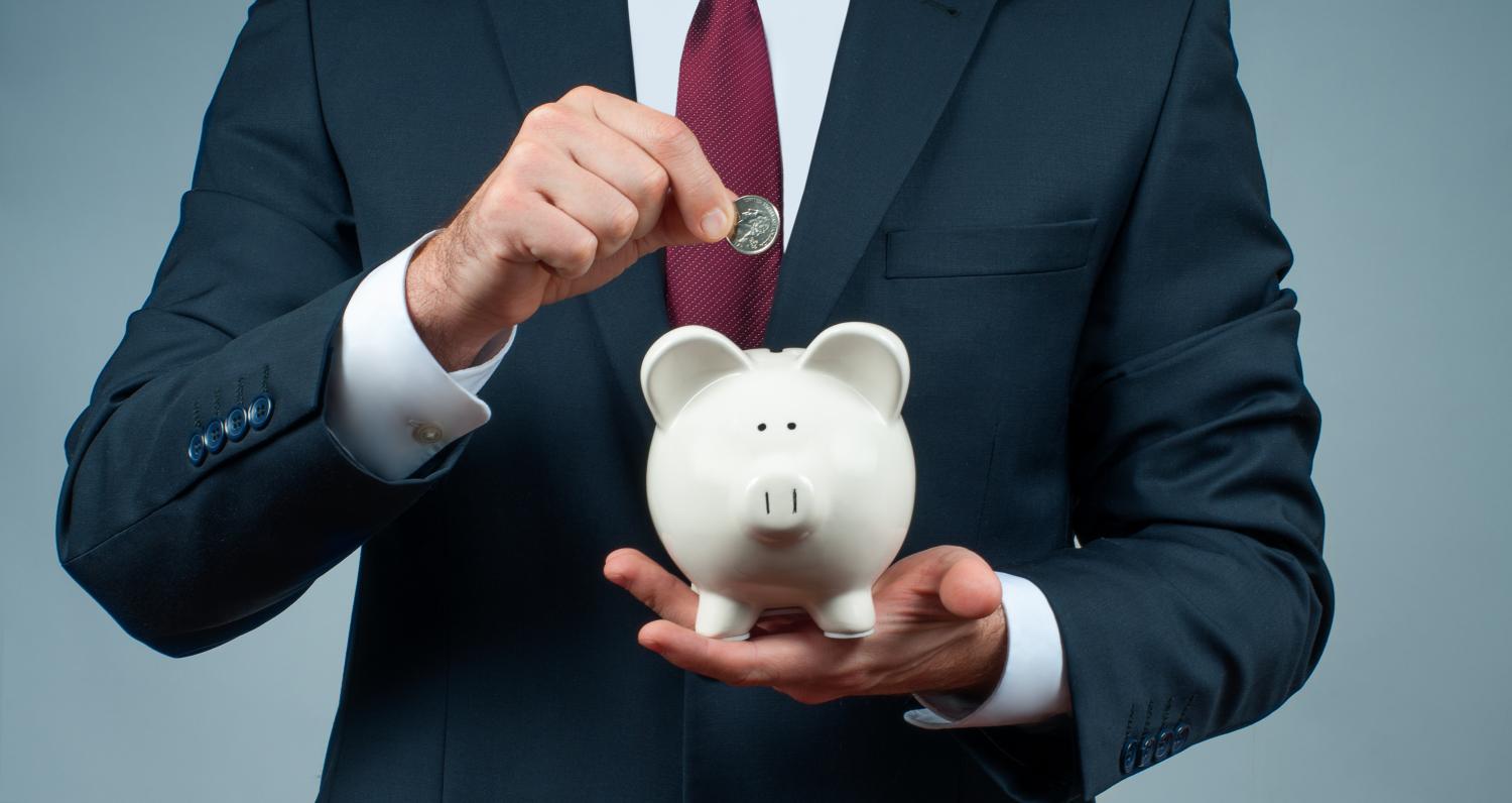 Man in a suit putting a coin into a piggy bank.