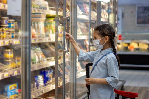 Young girl with surgical mask in freezer section of grocery store.