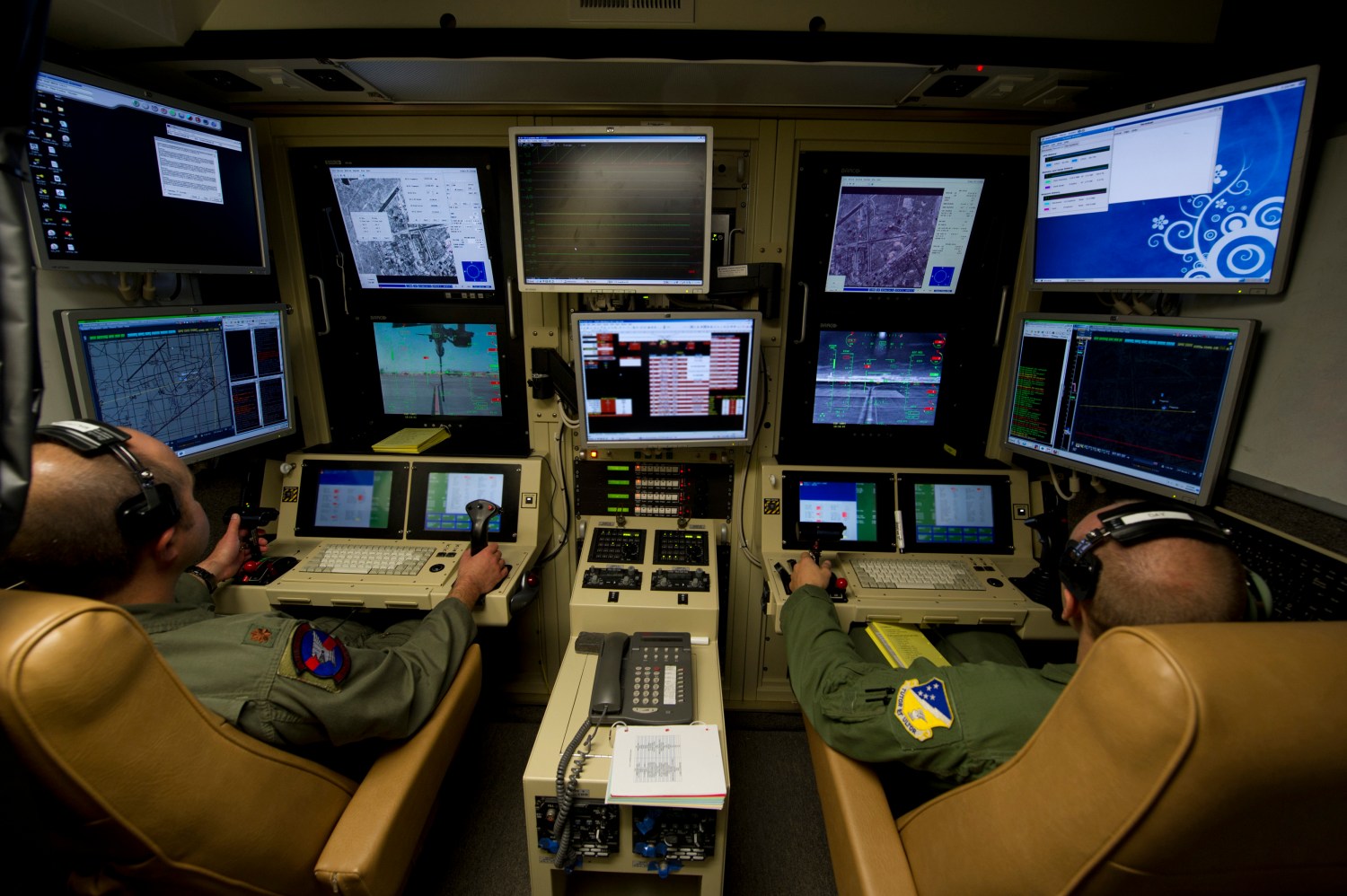 Two drone operators fly an MQ-9 Reaper drone from a remote station.