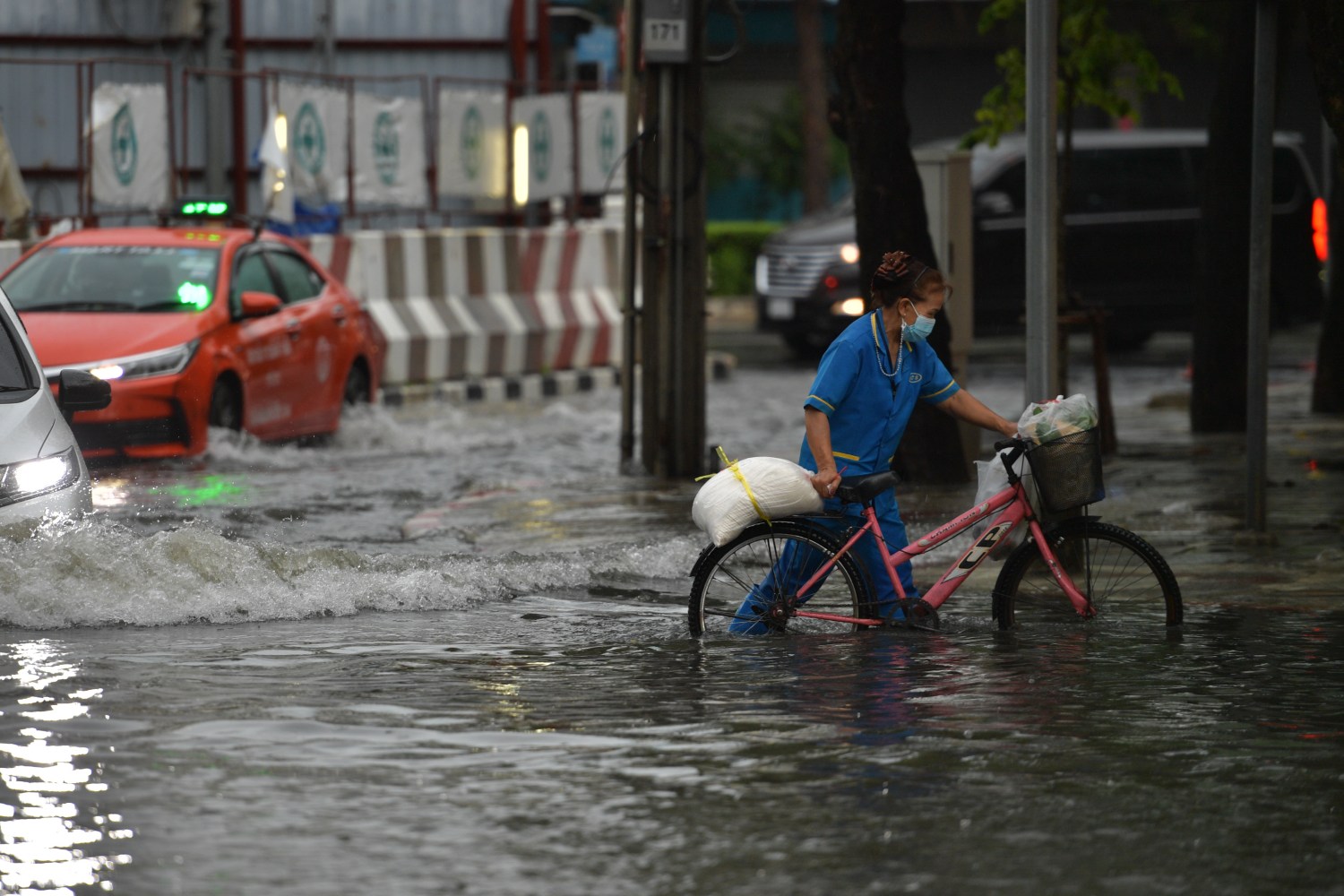 A woman is seen wearing a face mask pushes her bicycle through a water-logged road during a heavy rain in Bangkok on September 19, 2021 in Bangkok, Thailand. (Photo by Vachira Vachira/NurPhoto)NO USE FRANCE