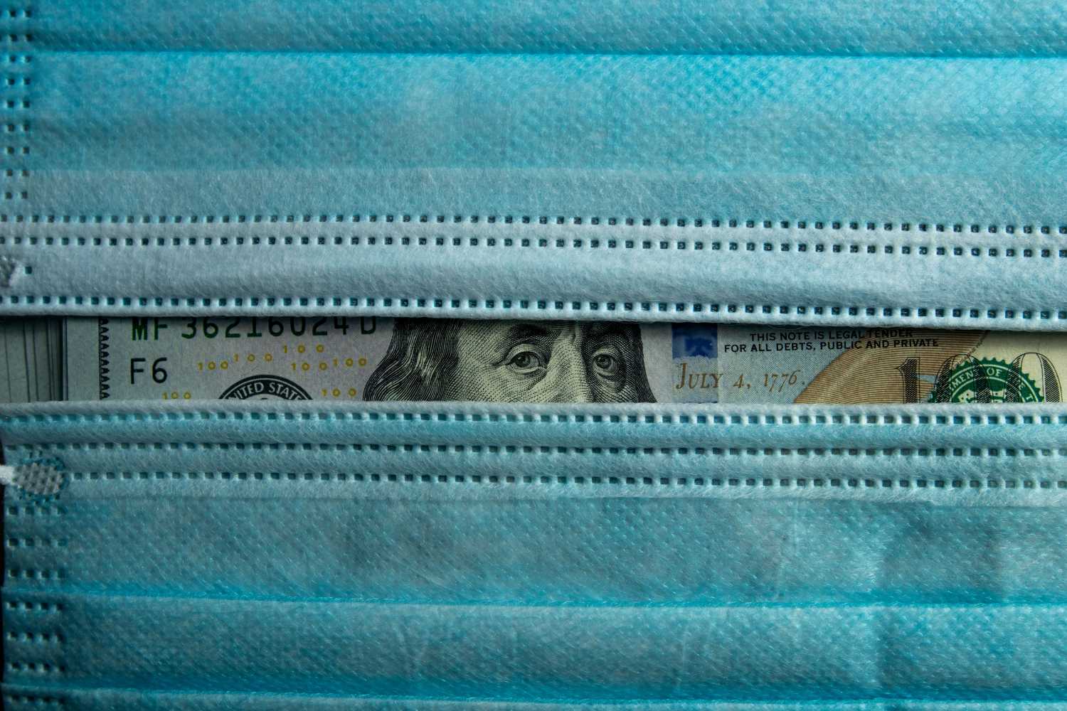 U.S. currency peeking out from behind two surgical masks
