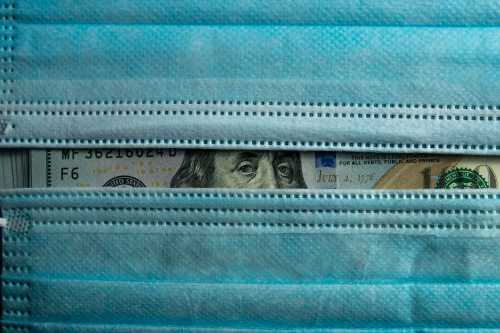 U.S. currency peeking out from behind two surgical masks