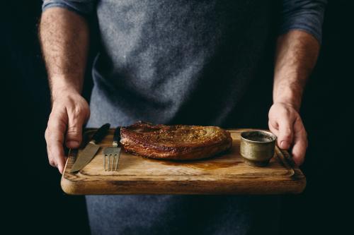 Man holding grilled beef steak with spices on cutting board