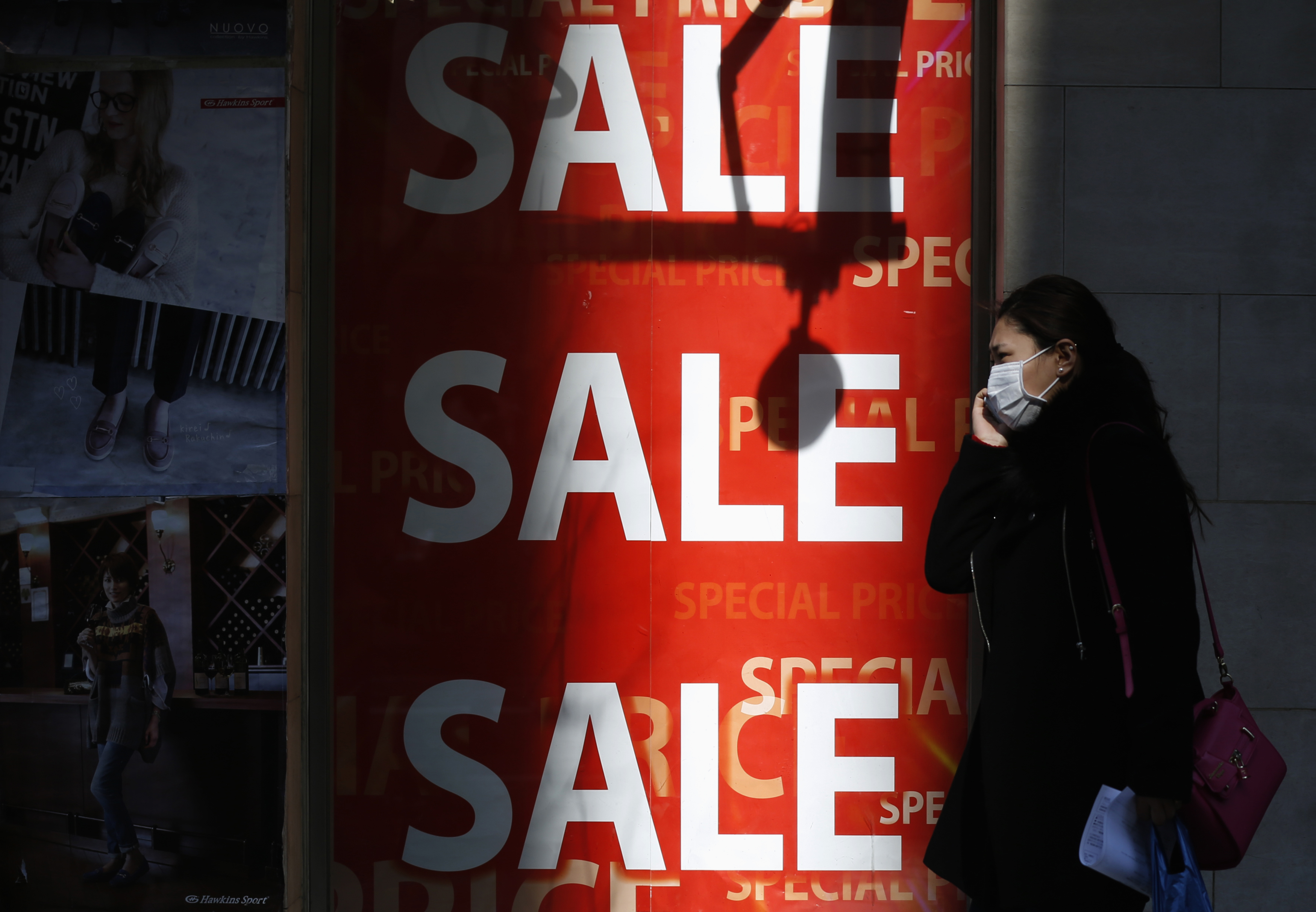 A woman holding her mobile phone walks past a sales advertisement poster in front of a shoe store in Tokyo February 15, 2015. Japan's economy rebounded from recession to grow an annualized 2.2 percent in the final quarter of last year, giving a much-needed boost to premier Shinzo Abe's efforts to shake off decades of stagnation even as the global outlook deteriorates. Picture taken February 15, 2015. REUTERS/Yuya Shino (JAPAN - Tags: BUSINESS POLITICS)