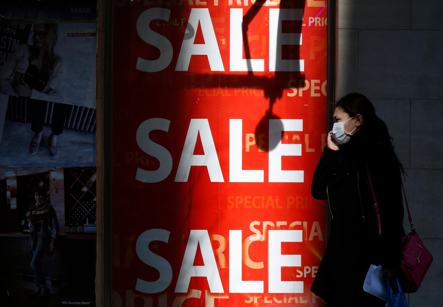 A woman holding her mobile phone walks past a sales advertisement poster in front of a shoe store in Tokyo February 15, 2015. Japan's economy rebounded from recession to grow an annualized 2.2 percent in the final quarter of last year, giving a much-needed boost to premier Shinzo Abe's efforts to shake off decades of stagnation even as the global outlook deteriorates. Picture taken February 15, 2015. REUTERS/Yuya Shino (JAPAN - Tags: BUSINESS POLITICS)
