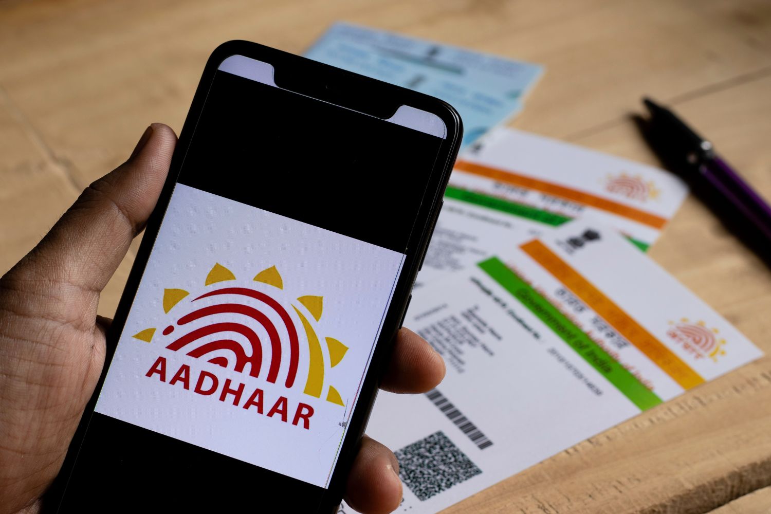 Birbhum, West Bengal / India - 18th August 2020: Aadhaar and PAN cards on wooden floor while a smart phone with mAadhaar app held in hand