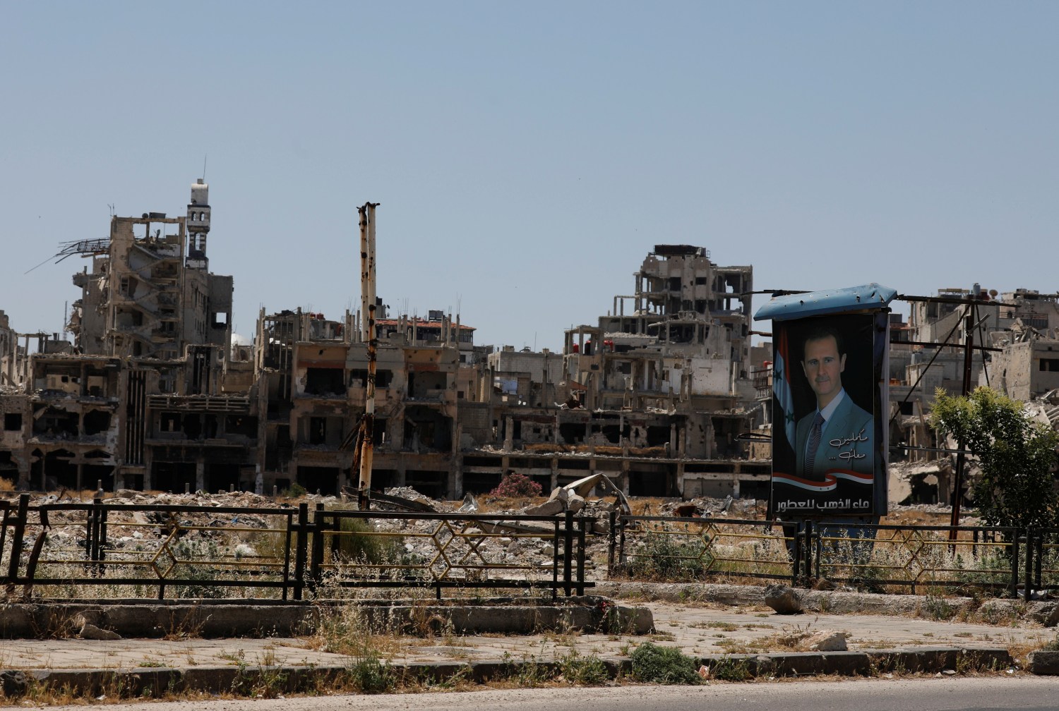 A poster depicting Syria's President Bashar al-Assad is pictured near damaged buildings, ahead of the May 26 presidential election, in Homs, Syria May 23, 2021. Picture taken May 23, 2021. REUTERS/Omar Sanadiki