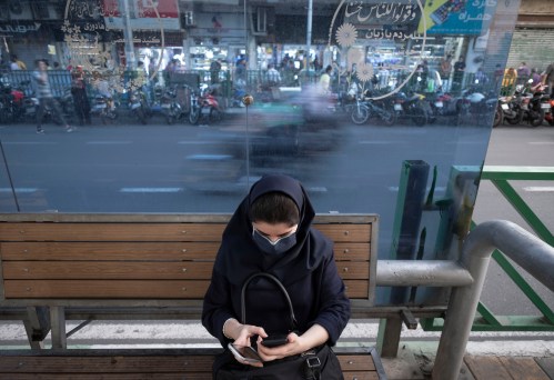 An Iranian woman wearing a protective face mask uses her smartphone while sitting at a bus-stand near a crossroad in downtown Tehran on May 30, 2021. Iranians will vote to elect the new President on June 18 amid the new corona virus outbreak in Iran.  (Photo by Morteza Nikoubazl/NurPhoto)NO USE FRANCE