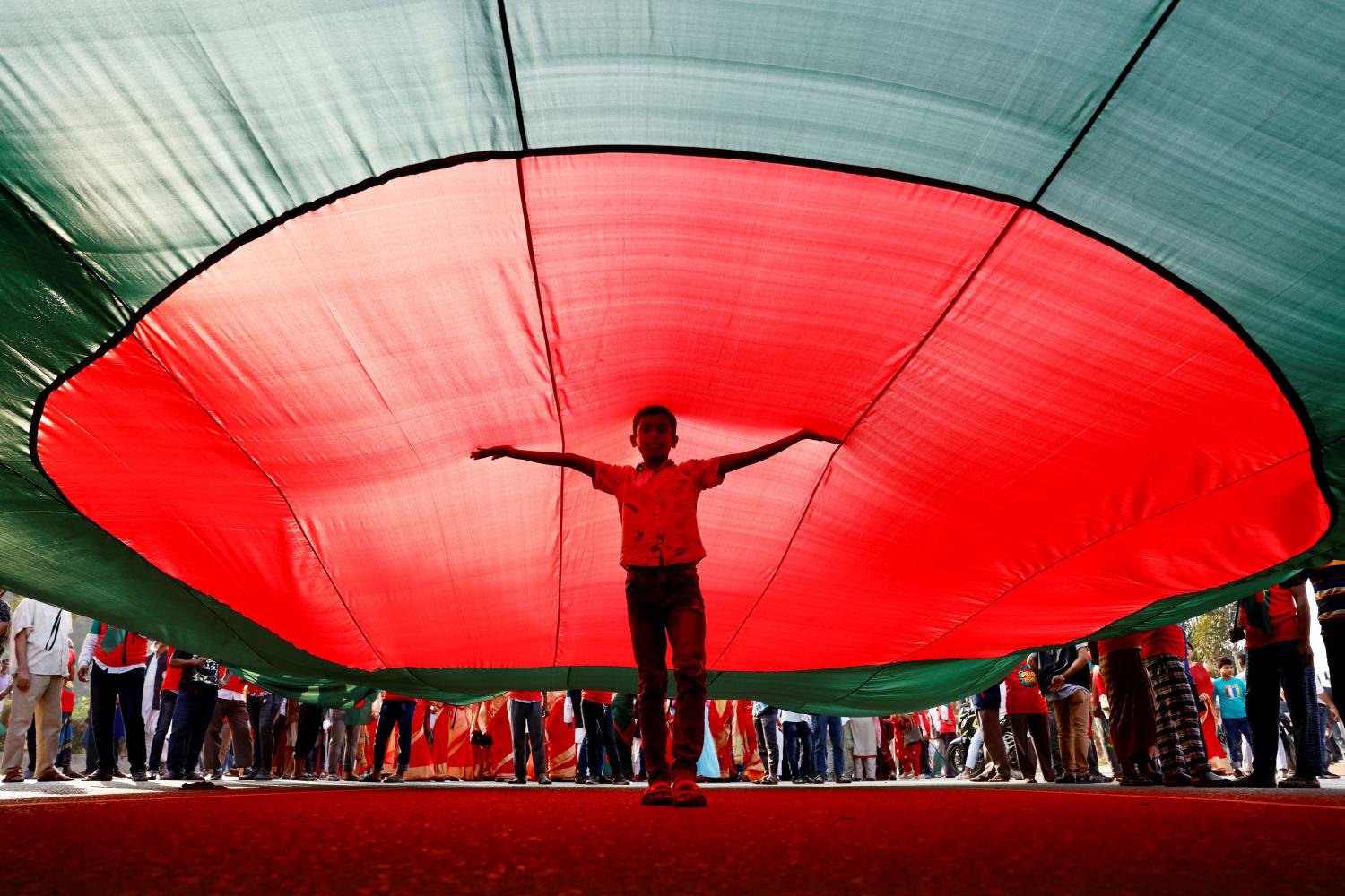 A boy poses for a picture under a massive Bangladeshi flag, during a flag rally three days ahead of the country's 50th Victory Day anniversary, in front of the parliamentary building in Dhaka, Bangladesh, December 13, 2021. REUTERS/Mohammad Ponir Hossain